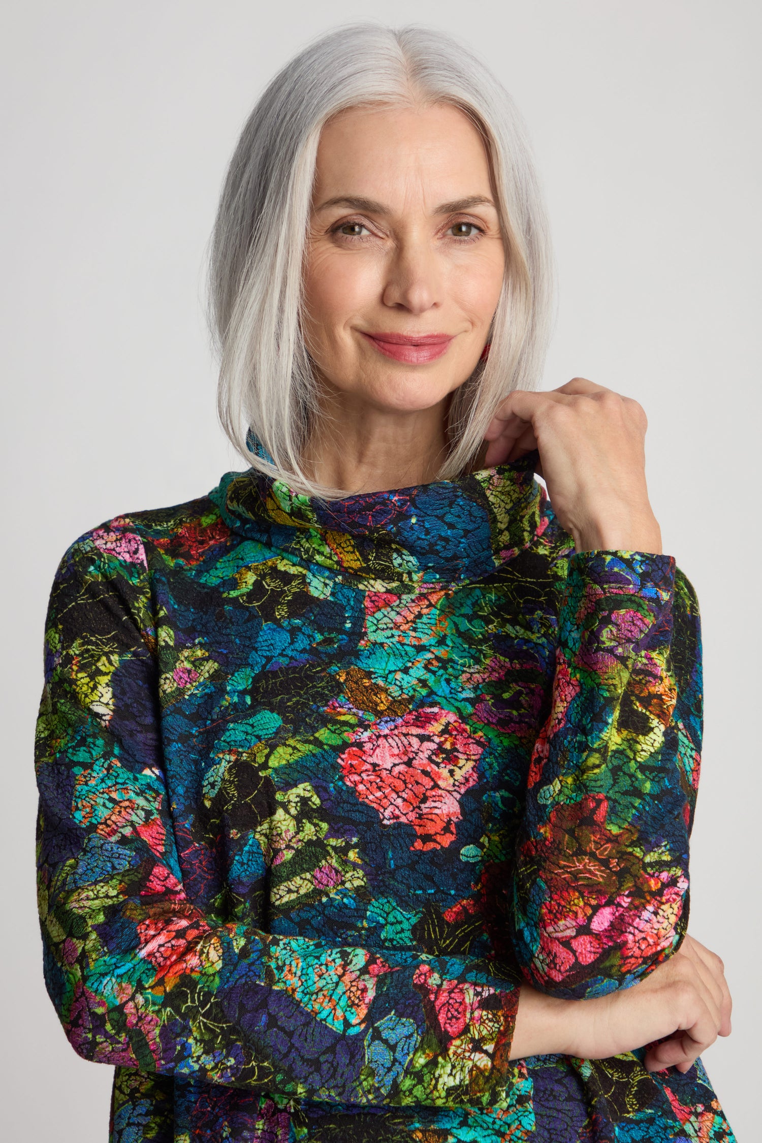 A woman with gray hair, wearing an Abstract Floral Jersey Cowl Neck Top, stands against a neutral background.