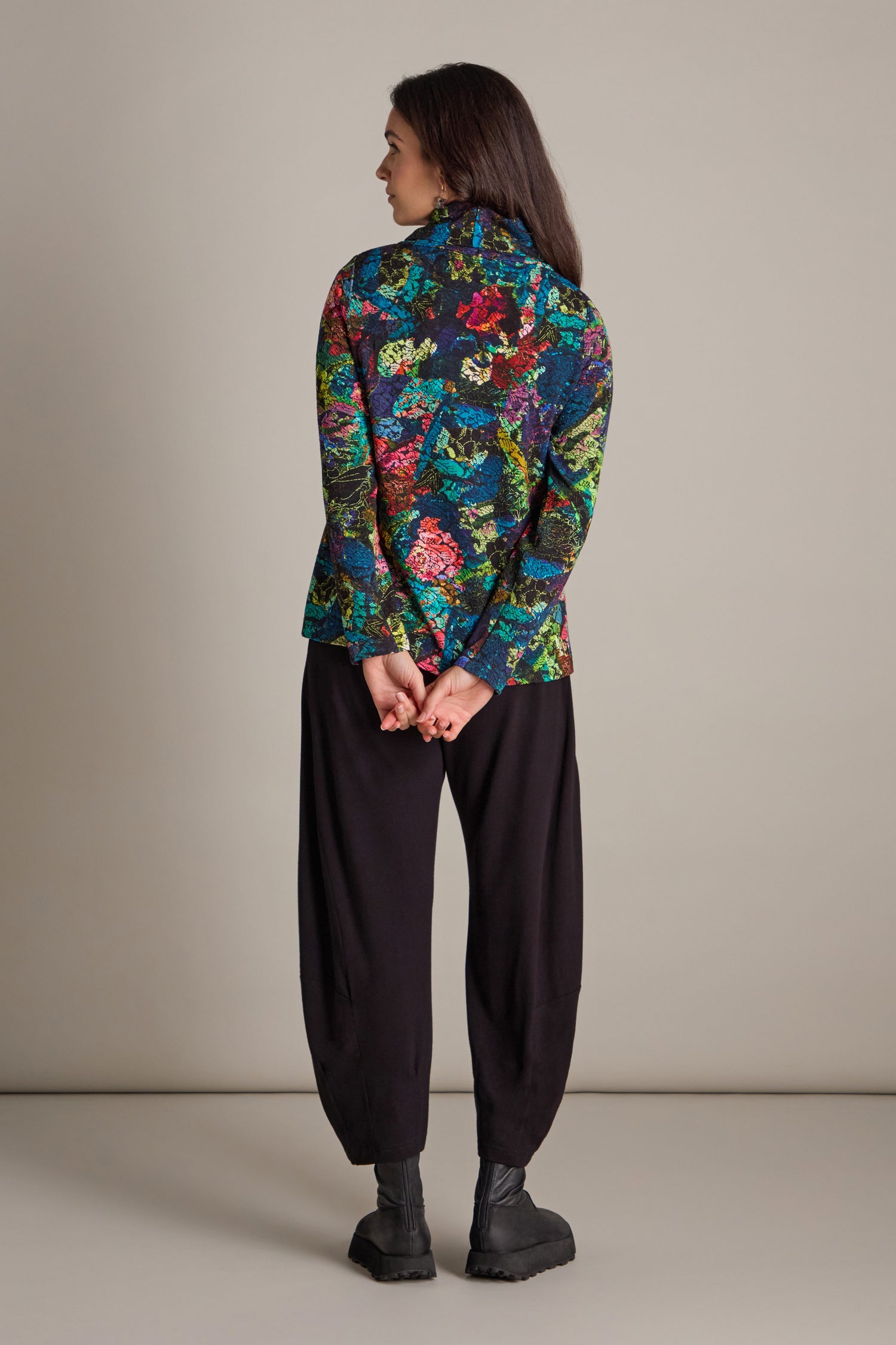 Person wearing an Abstract Floral Jersey Cowl Neck Top with black pants and shoes stands with hands clasped behind their back, facing away.