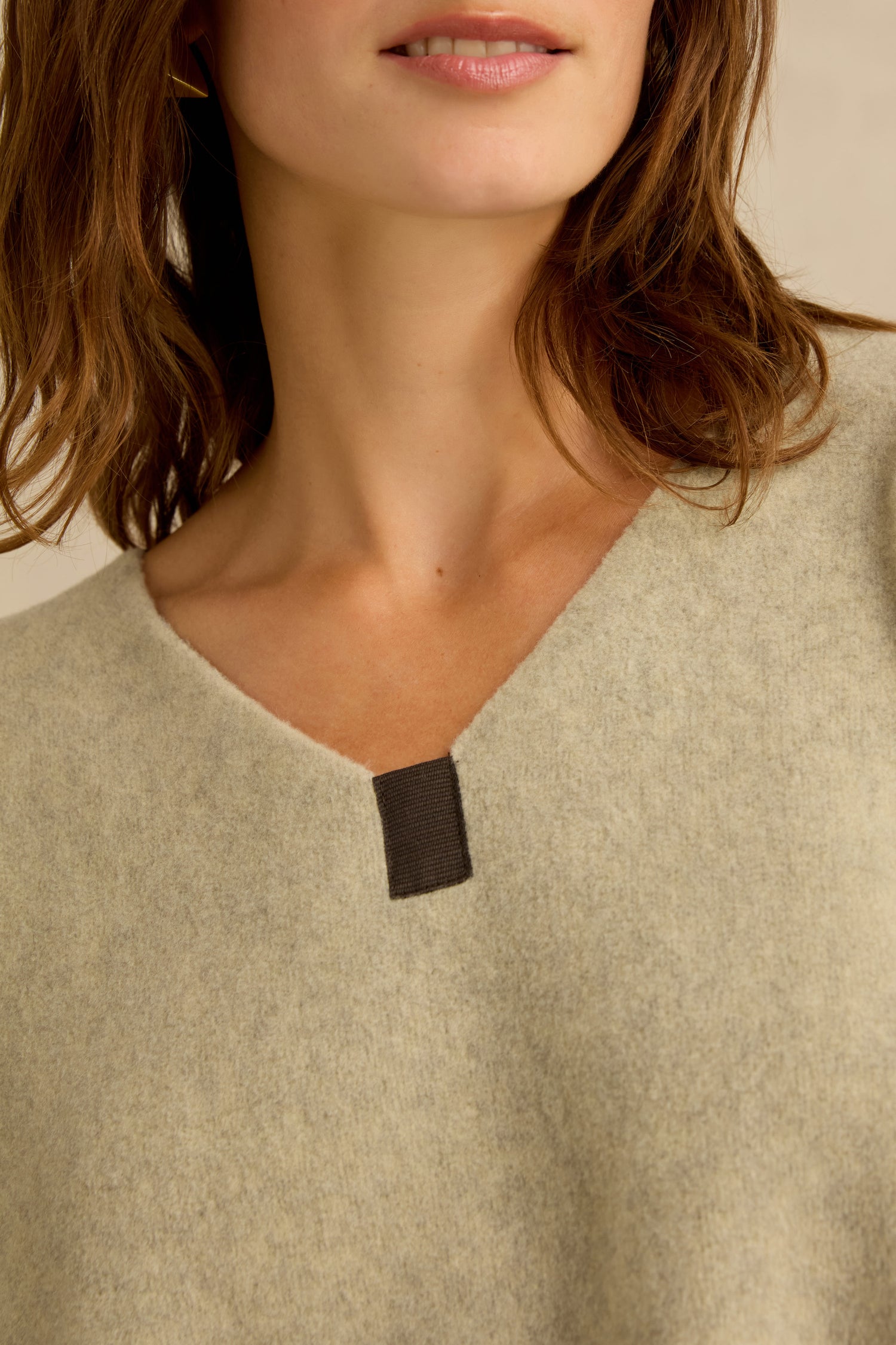 Close-up of a woman wearing a Cream Marl V Neck Fleece Tunic with a small black tab at the neckline. Only the lower face, neck, and part of the shoulder are visible.