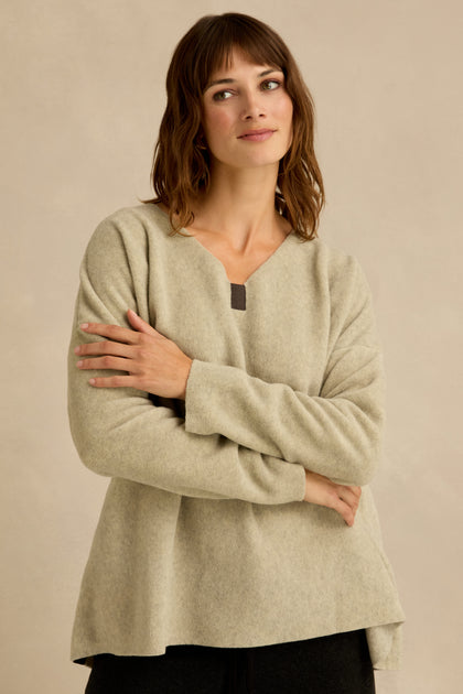 A person with shoulder-length brown hair wearing a light beige Cream Marl V Neck Fleece Tunic stands with arms crossed in front of a neutral background.
