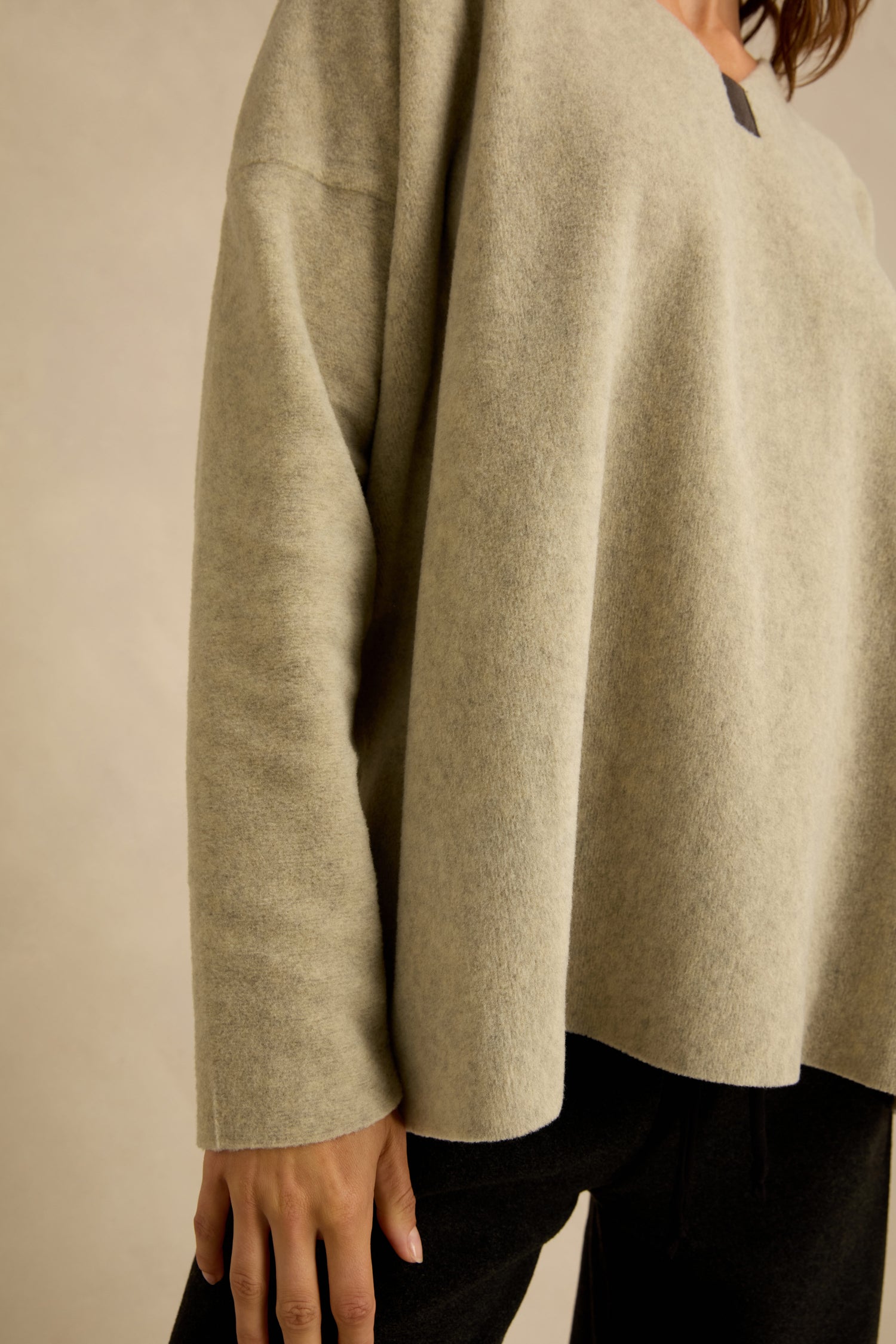 A person wearing a loose, light beige Cream Marl V Neck Fleece Tunic and black pants, shown from the shoulders down against a neutral background.