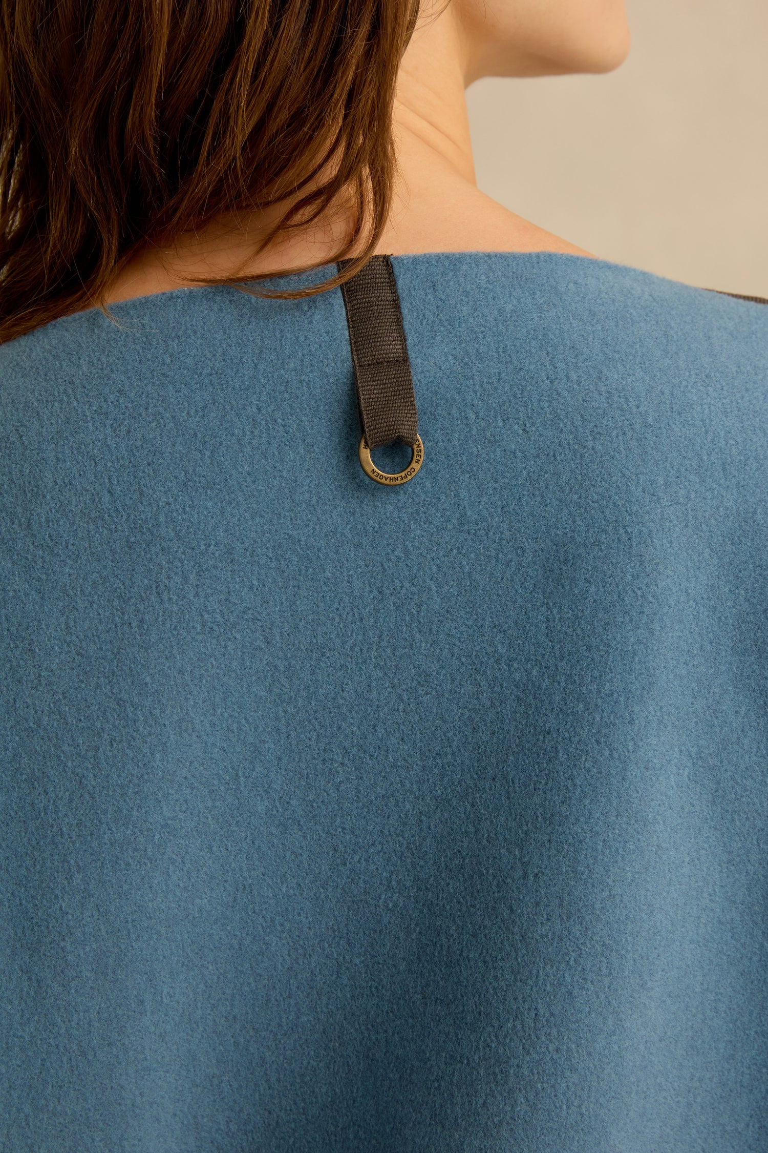 Close-up of a person wearing the Dusty Blue V Neck Fleece Tunic, featuring a black strap with a gold ring detail on the back near the neckline. This loose fit fleece offers comfortable styling and chic accents, perfect for those who love effortless fashion.