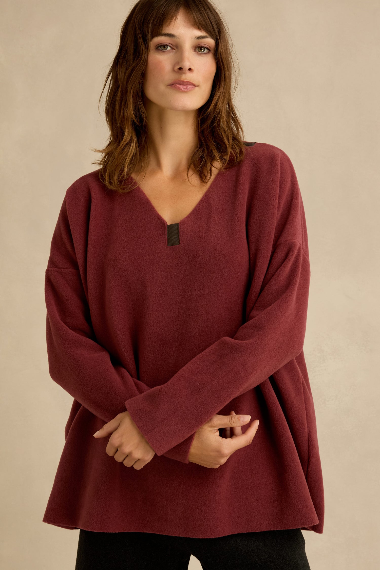 Woman wearing a loose-fitting, long-sleeve Dusty Pink V Neck Fleece Tunic, standing against a neutral beige background.