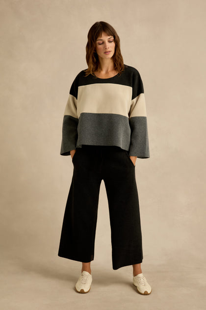A person wearing the Colour Block Fleece Boxy Top by Henriette Steffensen in black, cream, and gray, paired with wide-leg black pants and white sneakers, stands against a neutral background.