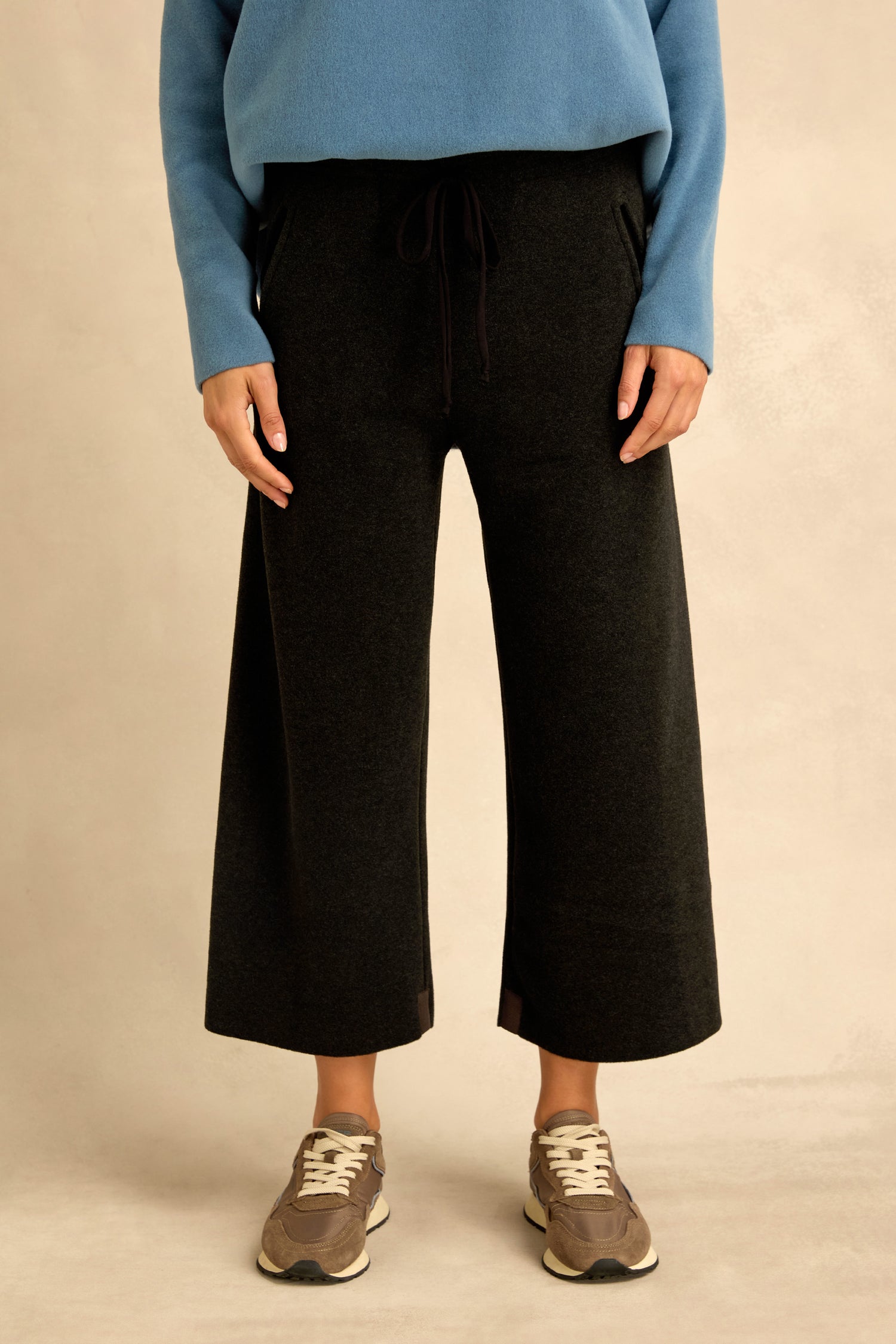 A person wearing a blue sweater, beige sneakers, and Straight Leg Fleece Trousers with a cropped length and drawstring stands against a light background.