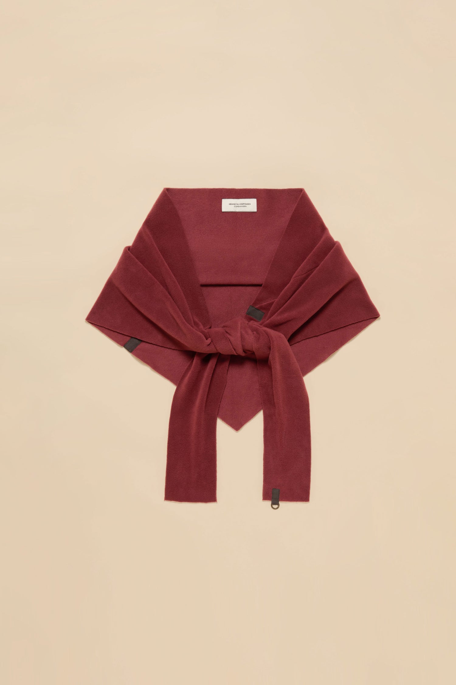 A folded maroon sweater, with its sleeves knotted at the front, rests on a beige background next to a Triangle Scarf.