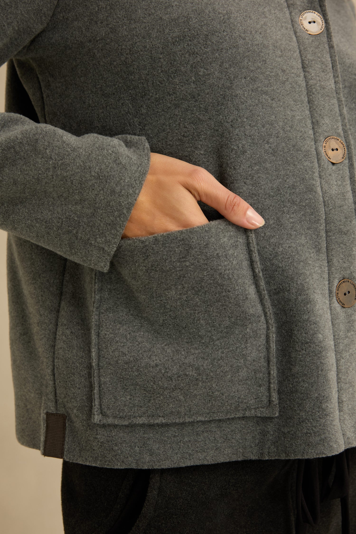 A person wearing the Grey Fleece Fitted Jacket places their hand inside a front pocket; the jacket features large buttons and a soft fleece texture.