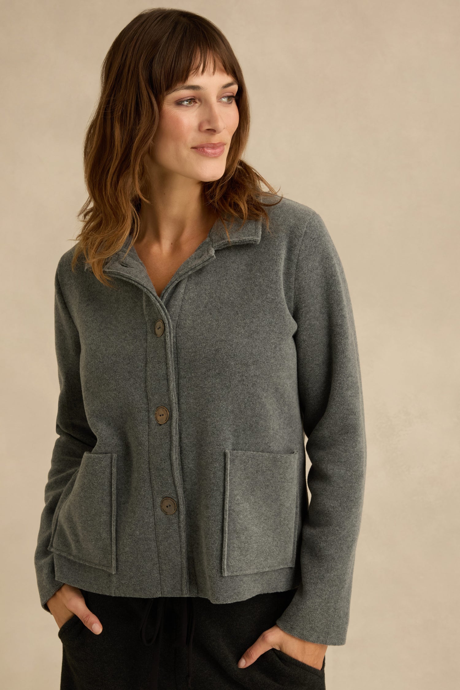 Woman wearing a Grey Fleece Fitted Jacket with front pockets, standing against a plain beige background and looking to the side.