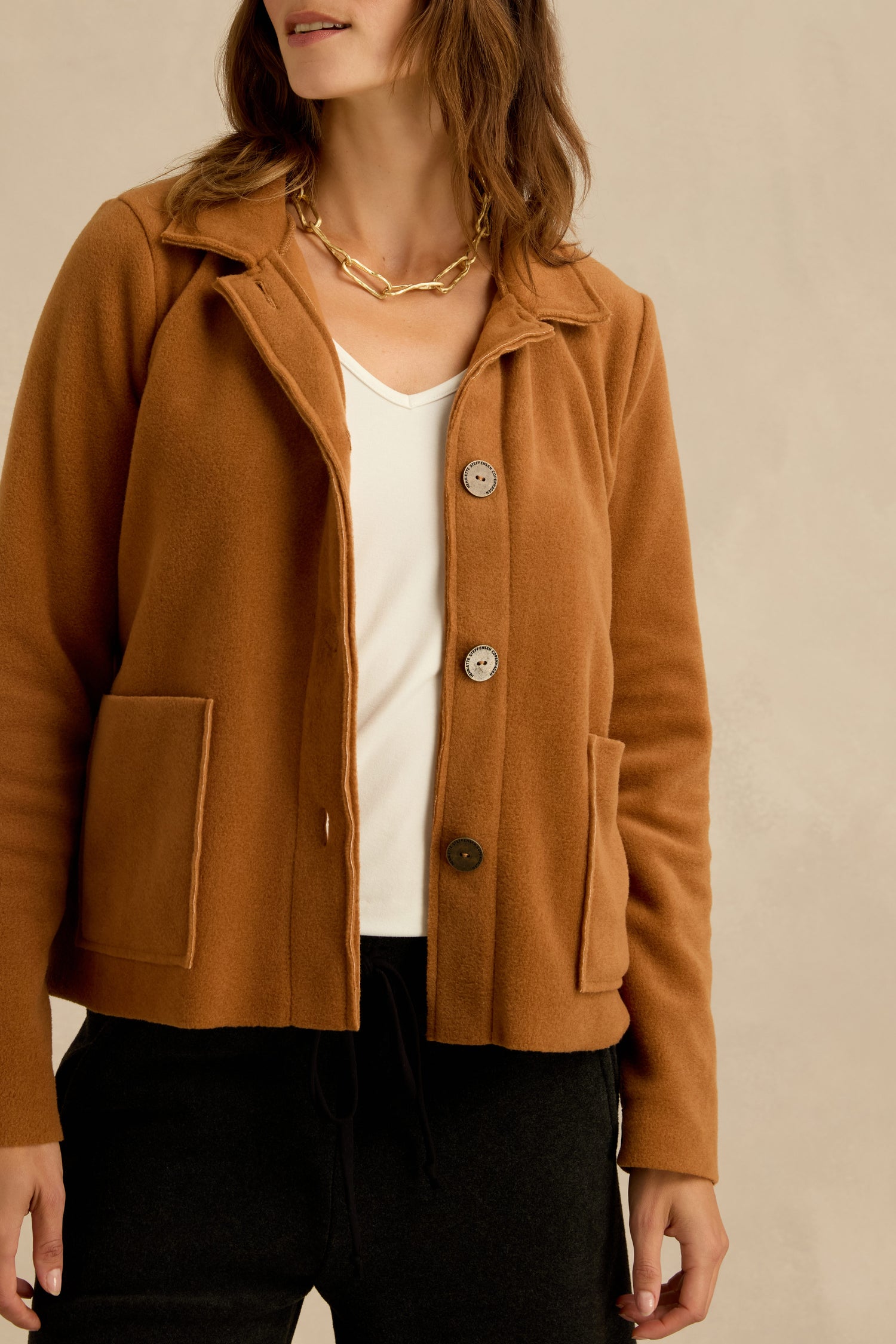 Woman wearing a Henriette Steffensen Rust Fleece Fitted Jacket over a white top and black pants, accessorized with a gold chain necklace, standing in front of a neutral background.