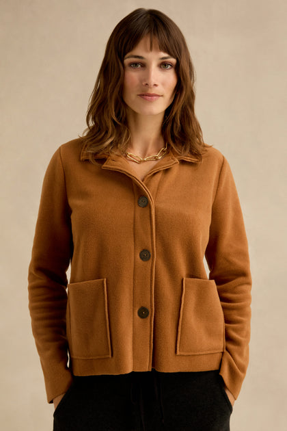 Woman standing against a neutral background, wearing a Rust Fleece Fitted Jacket with large front pockets and a gold chain necklace.