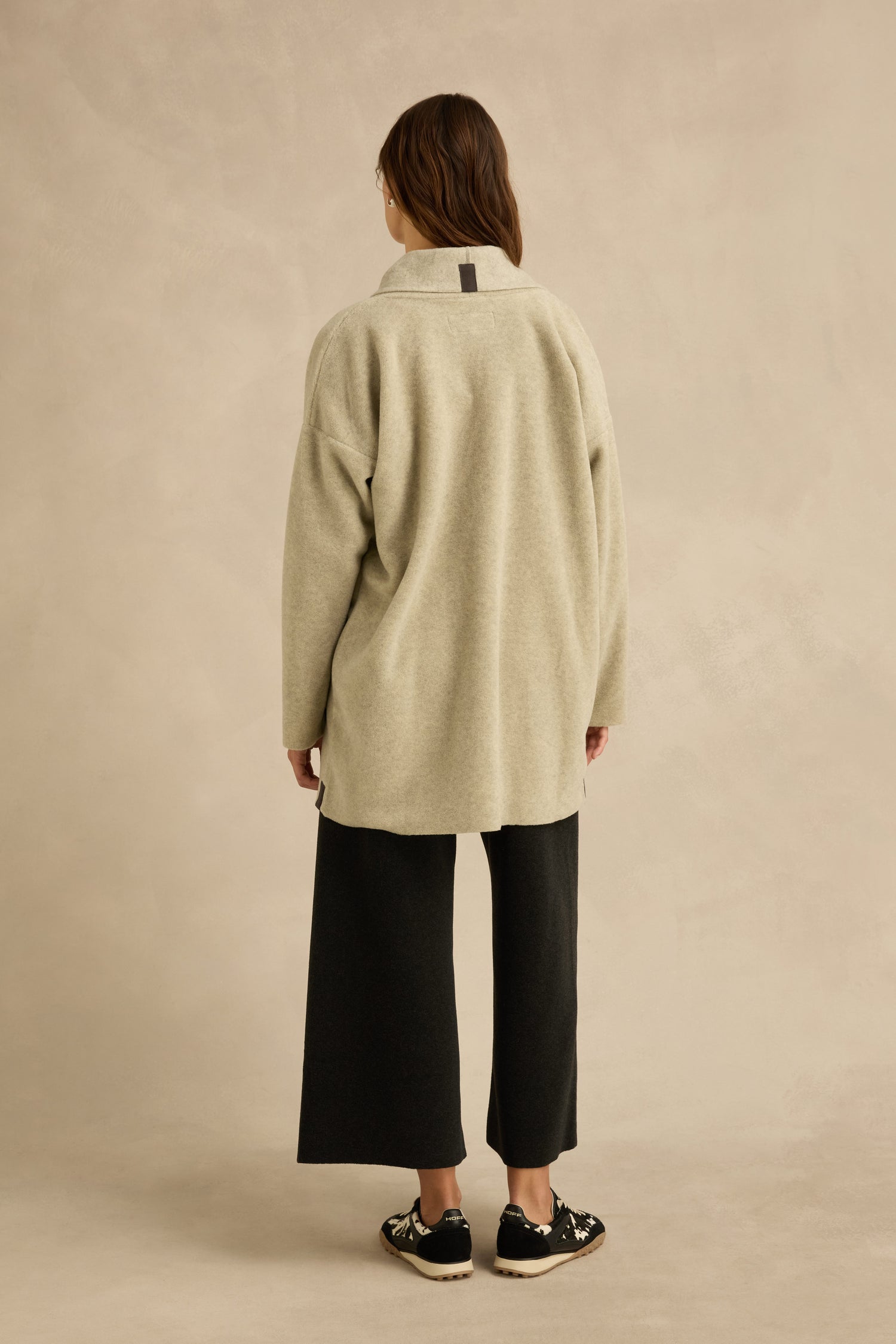 A person stands with their back to the camera, wearing the Cream Marl Fleece Cardigan with a relaxed fit, paired with wide-leg black pants and black sneakers, set against a neutral background.