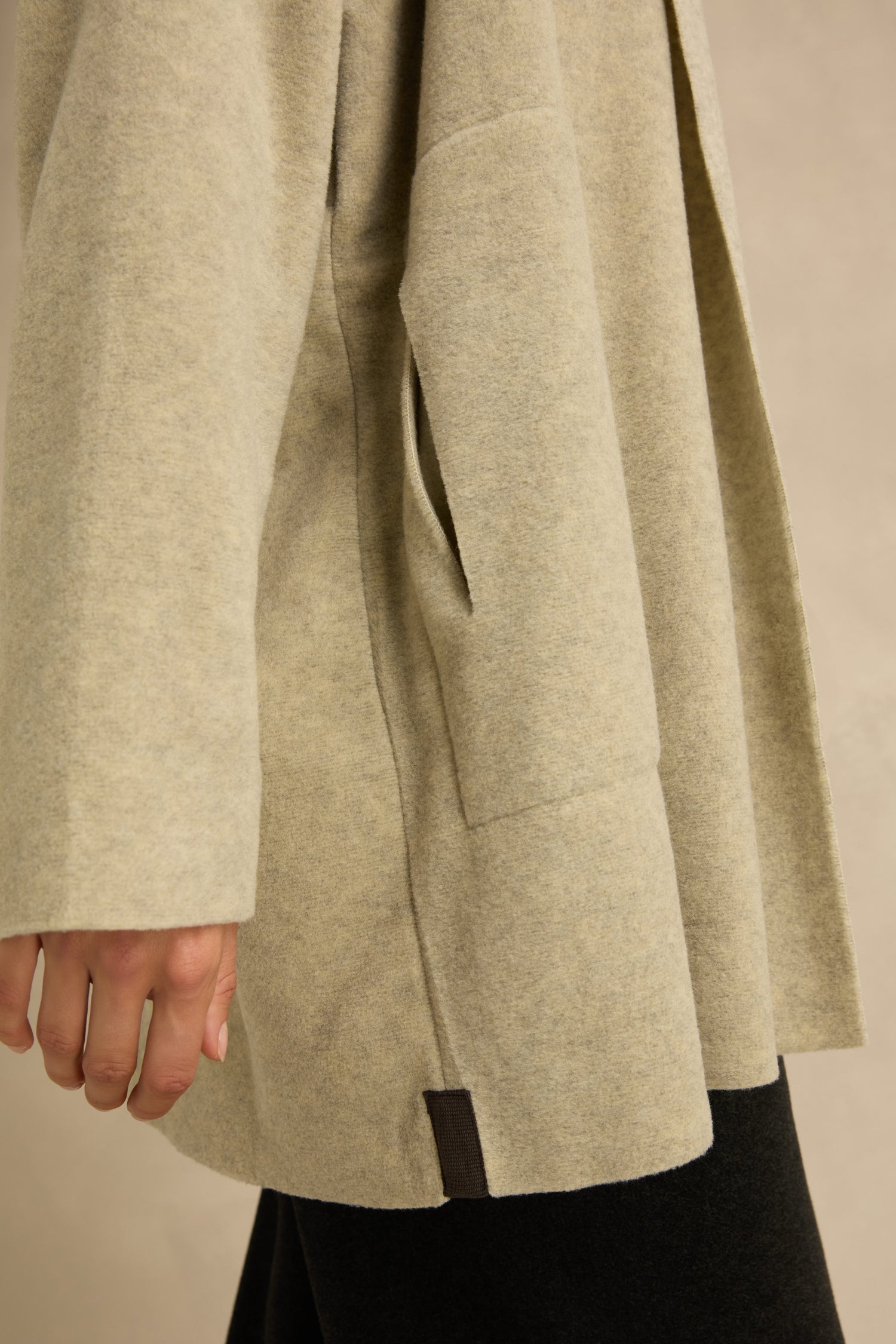Close-up of a person wearing the Cream Marl Fleece Cardigan with a pocket and relaxed fit, showing the left arm and part of black pants against a neutral background.