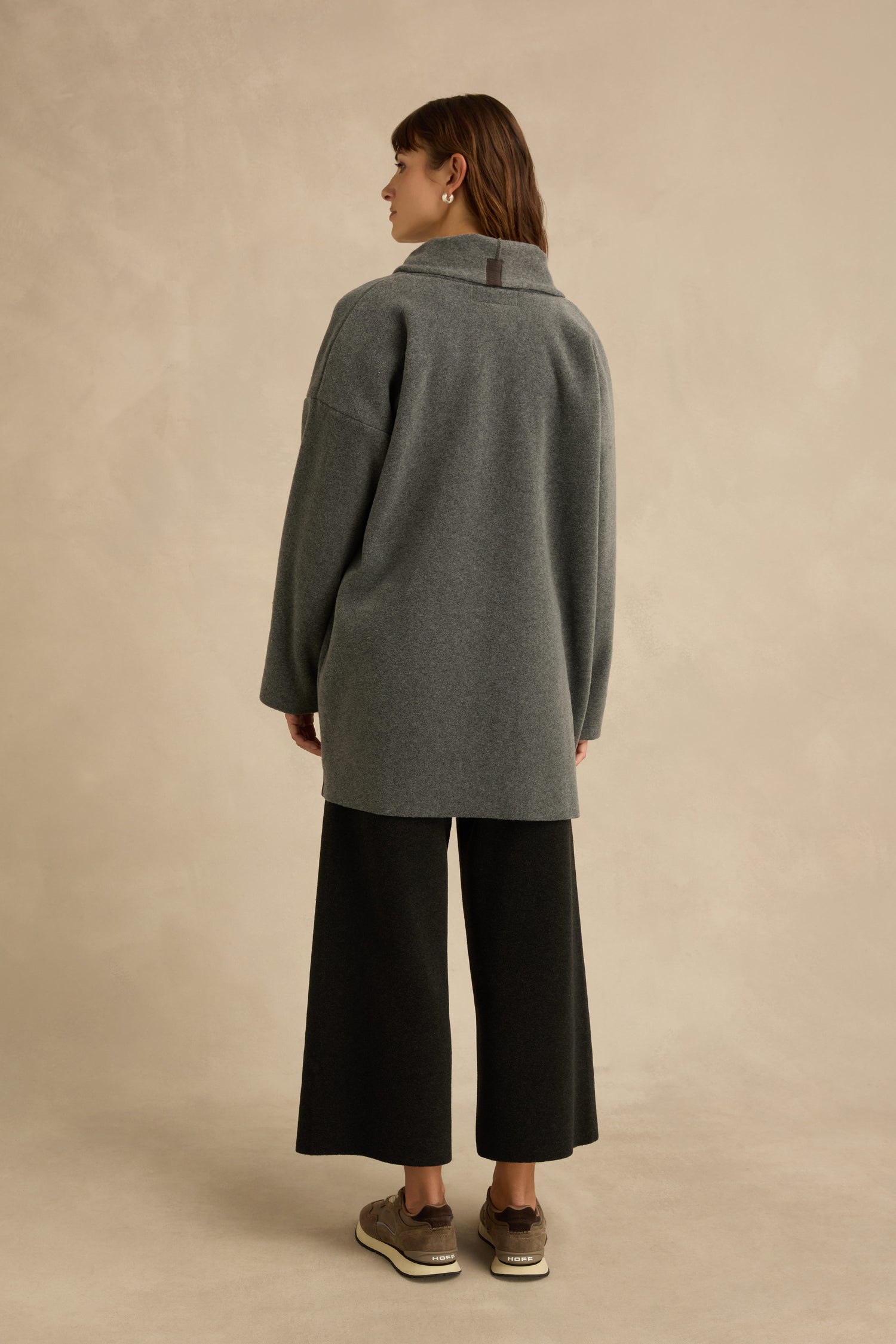 Person stands facing away, wearing the Grey Fleece Cardigan with wide-leg black pants and sneakers, against a plain beige backdrop.