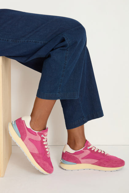 Someone sits on a light wooden bench against a plain background, wearing cropped blue jeans and City Retro Trainers with a memory foam insole.