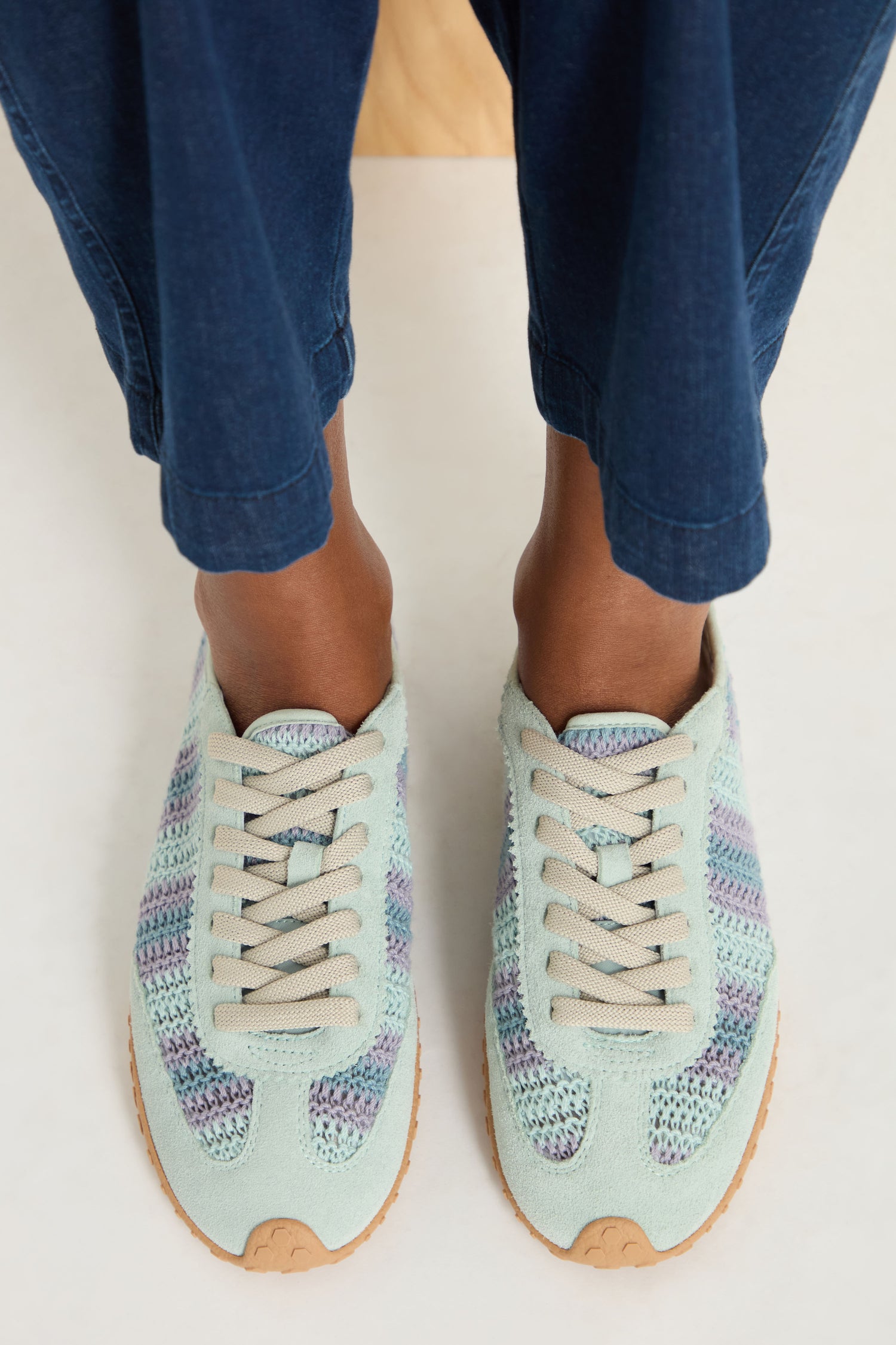 A person wearing light blue pants and Bridge Woven Light Blue Crochet Trainers with beige laces and cushioned sole stands on a white surface.