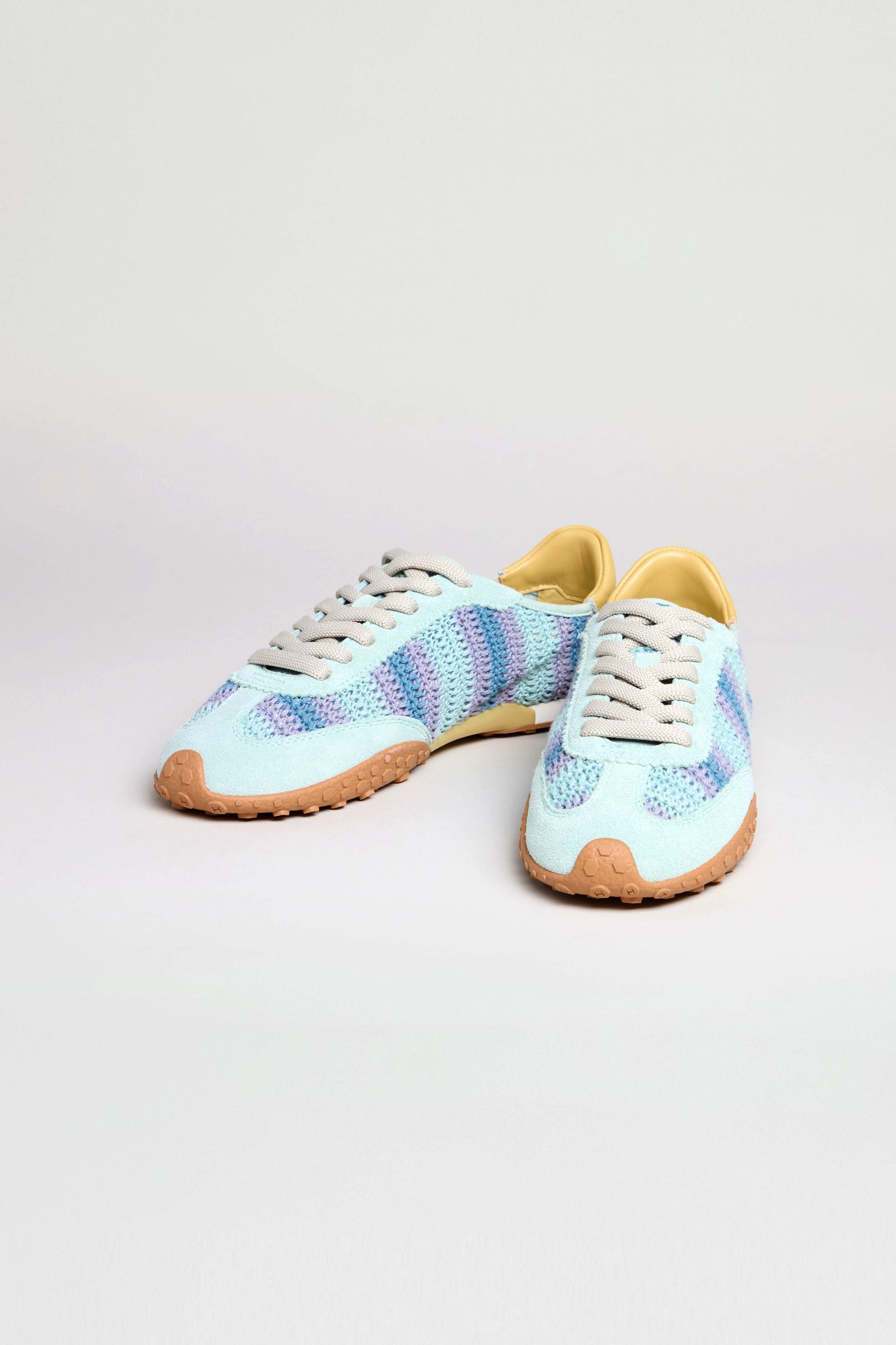 The Bridge Woven Light Blue Crochet Trainers feature blue and purple stripes, white laces, tan rubber soles, and a cushioned sole for all-day comfort, shown on a plain white background.