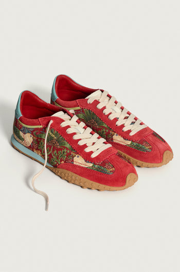 The Red William Morris Bridge Trainers are women’s red low-top leather sneakers with white laces, tan soles, and embroidered floral and bird motifs inspired by the Strawberry Thief print on the sides.