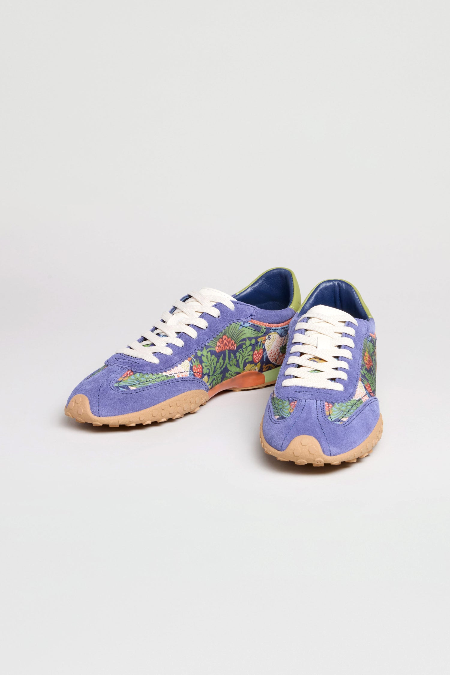 A pair of William Morris Bridge Trainers in purple with white laces, a floral Strawberry Thief print on the sides, and tan rubber soles displayed on a plain light background.