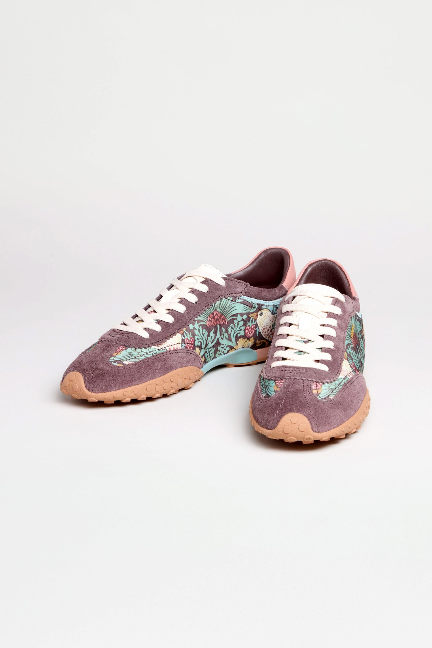 The William Morris Bridge Trainers are purple women's leather sneakers with white laces, tan soles, and a Strawberry Thief print floral pattern on the sides, shown against a plain light background.