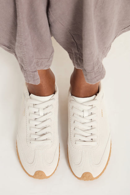 Person wearing Bridge Suede Trainers in a light color with loose grayish pants, viewed from above.