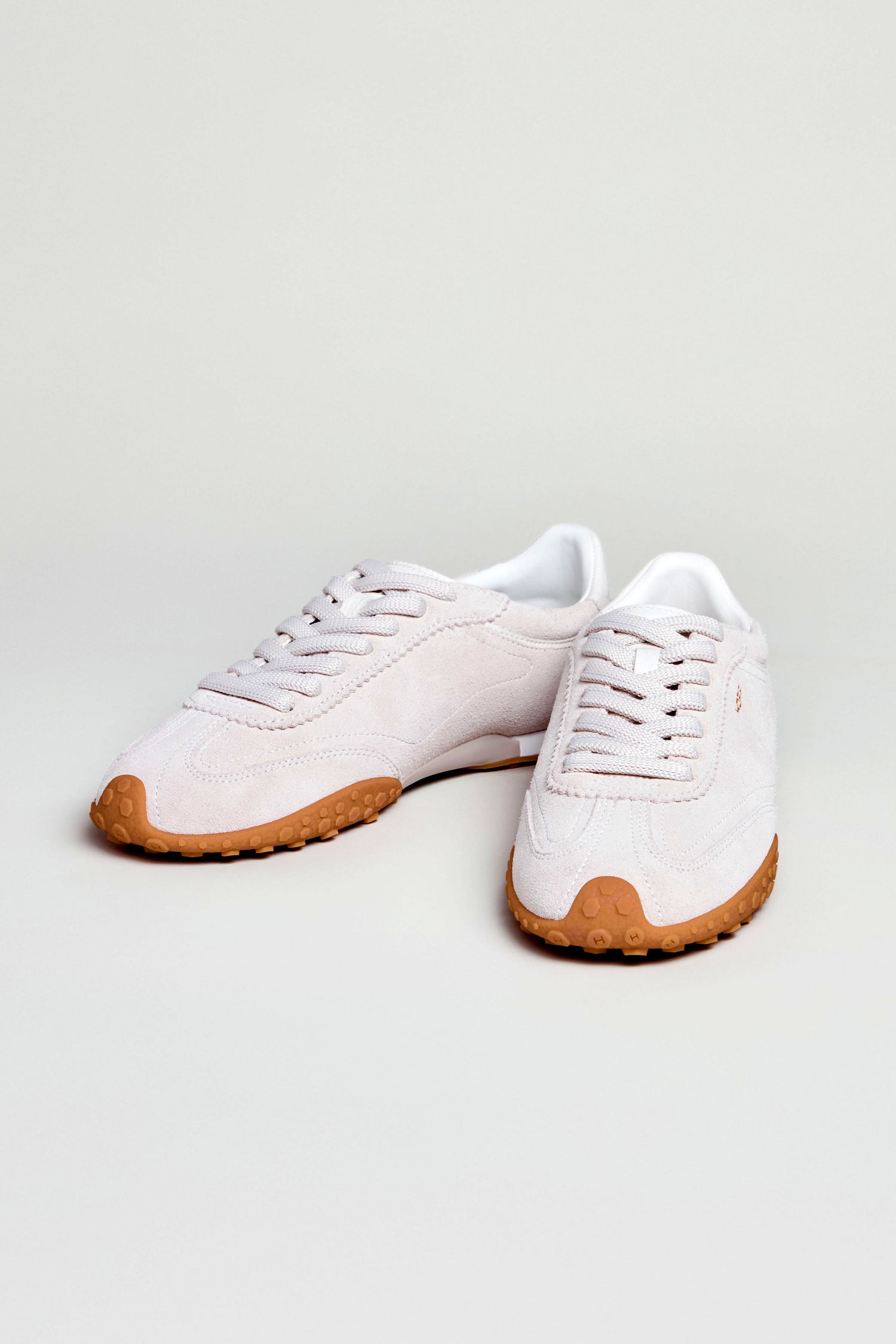 Bridge Suede Trainers in light pink suede feature white laces and tan rubber soles, offering a retro running style look. Displayed on a plain light background.