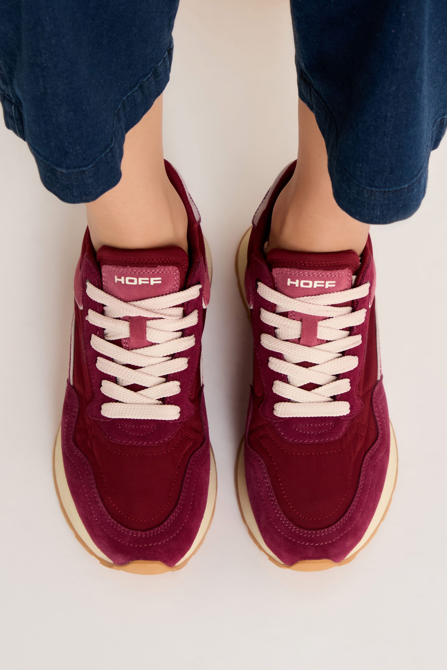 A person wearing City Trainers—premium maroon suede sneakers with white laces and gum soles—stands on a light surface, viewed from above.