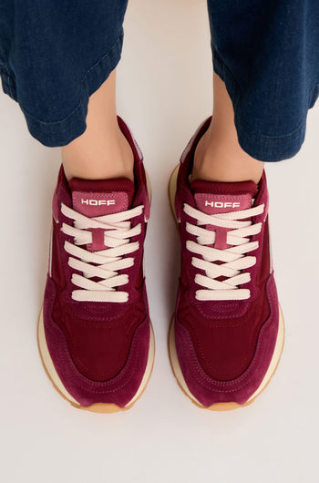 A person wearing City Trainers—premium maroon suede sneakers with white laces and gum soles—stands on a light surface, viewed from above.