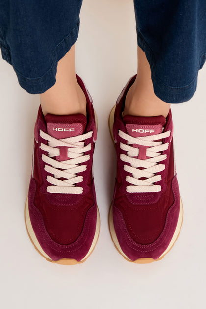 A person wearing City Trainers—premium maroon suede sneakers with white laces and gum soles—stands on a light surface, viewed from above.