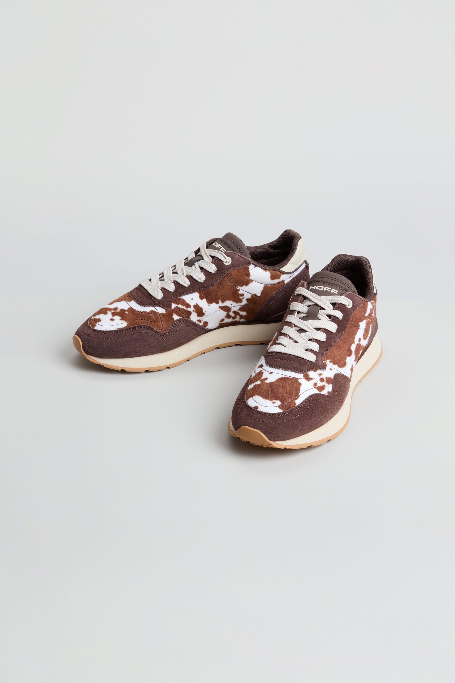 Animal Print City Trainers in a brown and white cowhide print, crafted with a premium suede finish, featuring white laces and light-colored soles, displayed on a plain background.