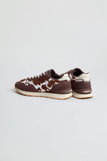 A pair of Animal Print City Trainers featuring a distinctive brown and white cowhide pattern, premium suede accents, brown soles, and "HOPE" branding on the back heels, displayed against a plain light background.