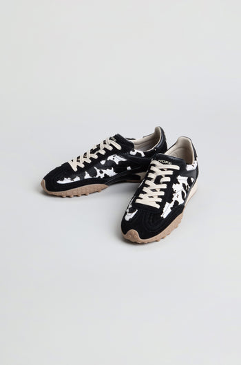 A pair of Animal Print Bridge Trainers featuring a black and white camo pattern in low-top suede, beige laces, and tan rubber soles, displayed on a plain light background.