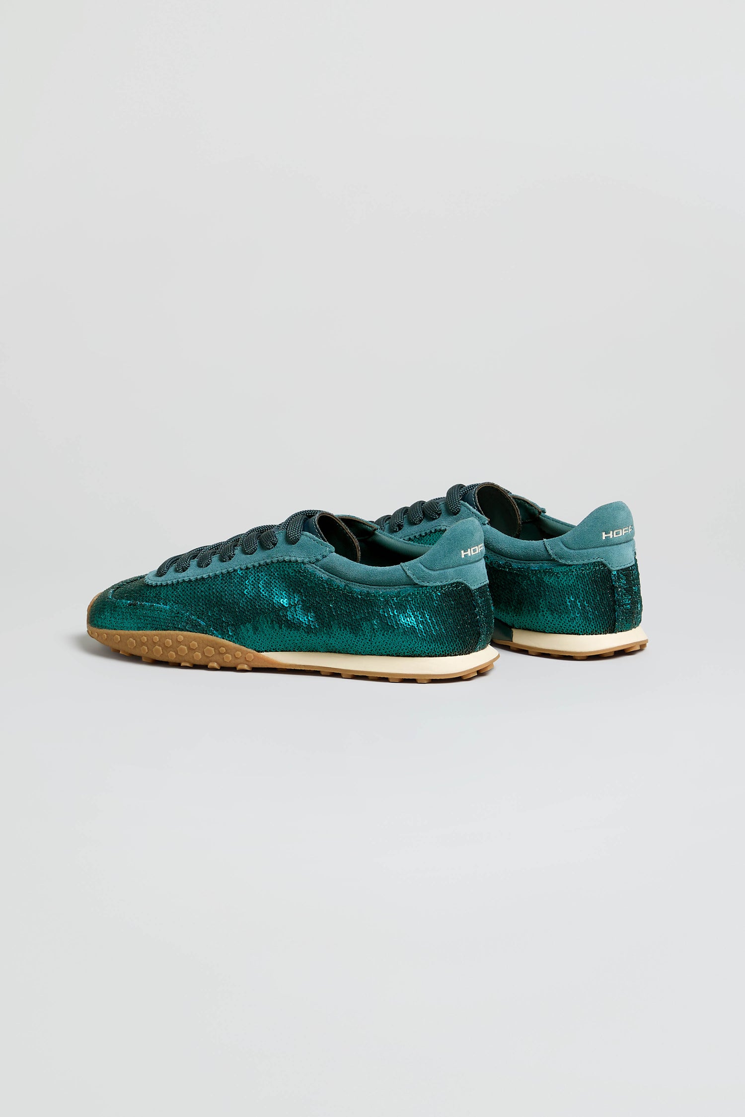 A pair of Sequin Bridge Trainers in teal-green suede, featuring a textured pattern, black laces, and light tan rubber soles, is displayed against a plain light background.