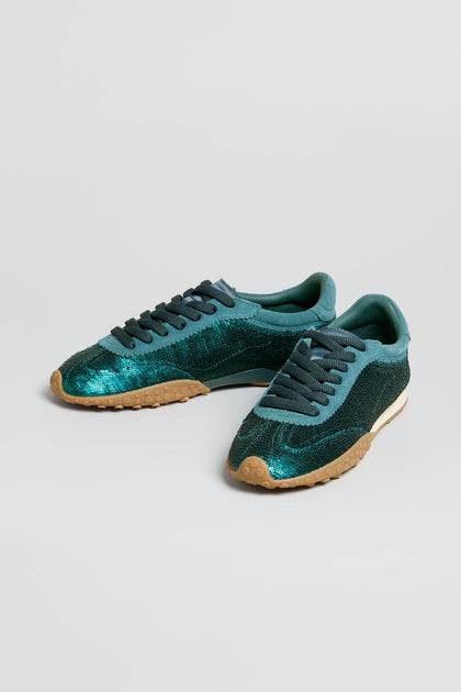 A pair of Sequin Bridge Trainers in teal glitter sequin, featuring dark teal laces, beige rubber soles, and a plush memory-foam insole, displayed on a plain white background.