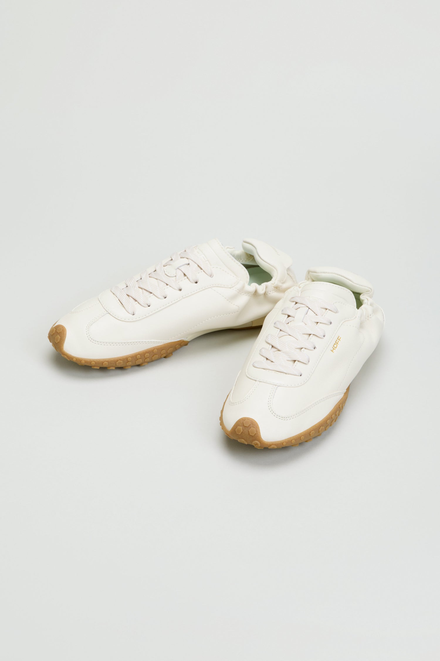A pair of Napa Leather Bridge Trainers in white, featuring low-top design, lace-up closures, and gum rubber outsoles, displayed against a plain light gray background.