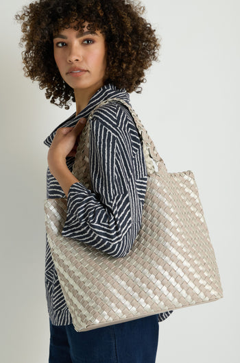 Woman with curly hair in a striped shirt and dark pants carries the Woven Reversible Grey & Silver Bag over her shoulder.