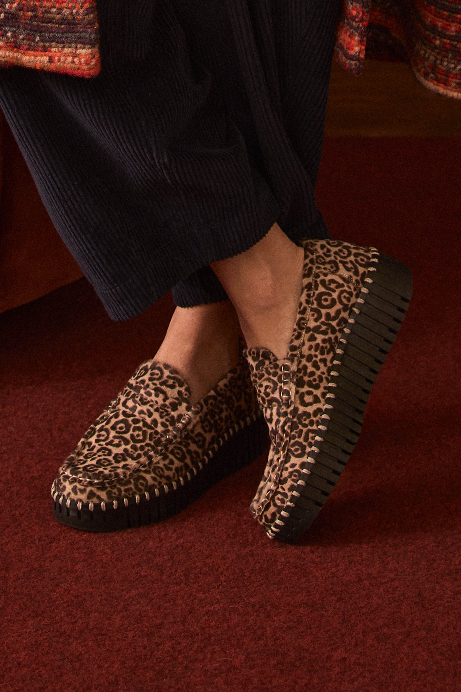 Wearing the Tulip Leopard Penny Loafers—an online exclusive with a thick black sole—paired with black pants, this effortlessly stylish look (style code IJTULIP3225) stands out as they sit cross-legged on a red carpeted floor.