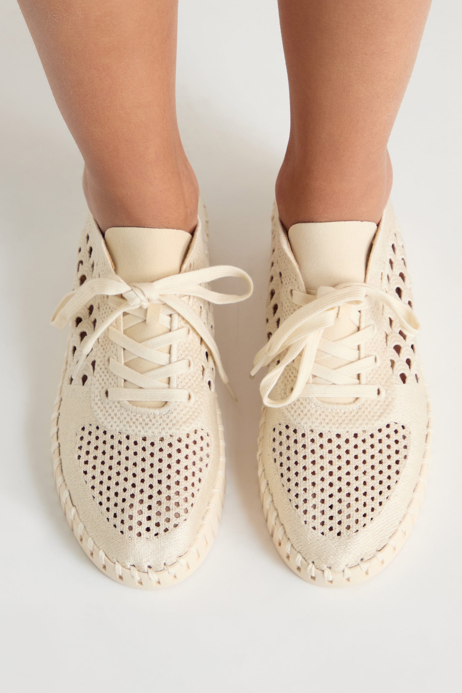 A pair of feet in cream Tulip Embroidered Platform Lace Up Trainers featuring perforations and woven details, photographed from above on a light background.