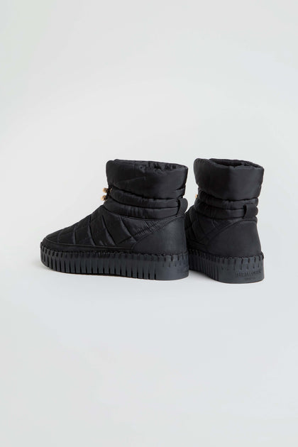 A pair of Tulip Quilted Winter Boots in black, featuring thick, cushioned soles and ridged tread, displayed from the back and side on a plain white background.