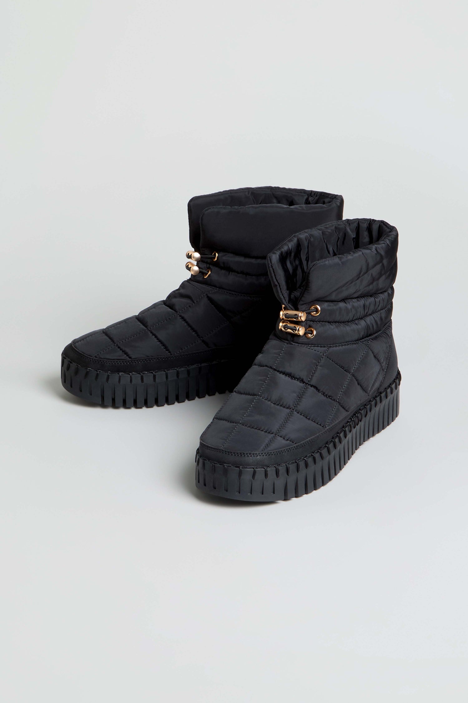 Tulip Quilted Winter Boots in black, featuring gold eyelet details and thick, cushioned rubber soles, displayed on a light gray background.