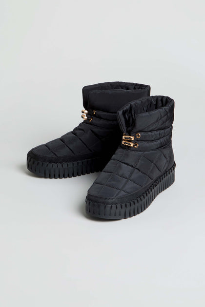 Tulip Quilted Winter Boots in black, featuring gold eyelet details and thick, cushioned rubber soles, displayed on a light gray background.