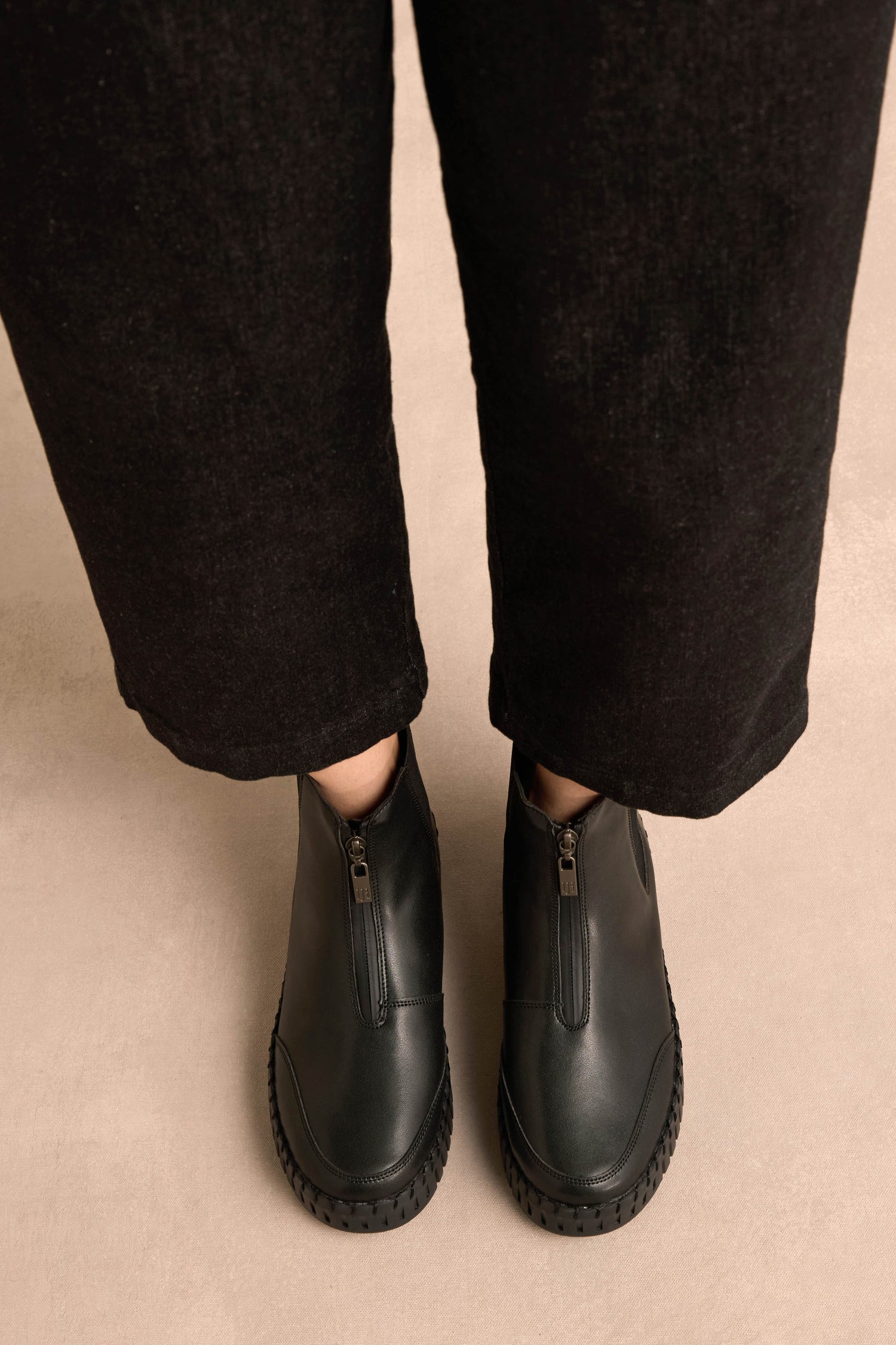 Person wearing black pants and Tulip Zip Chelsea Boots with faux shearling lining, standing on a beige floor, viewed from above.