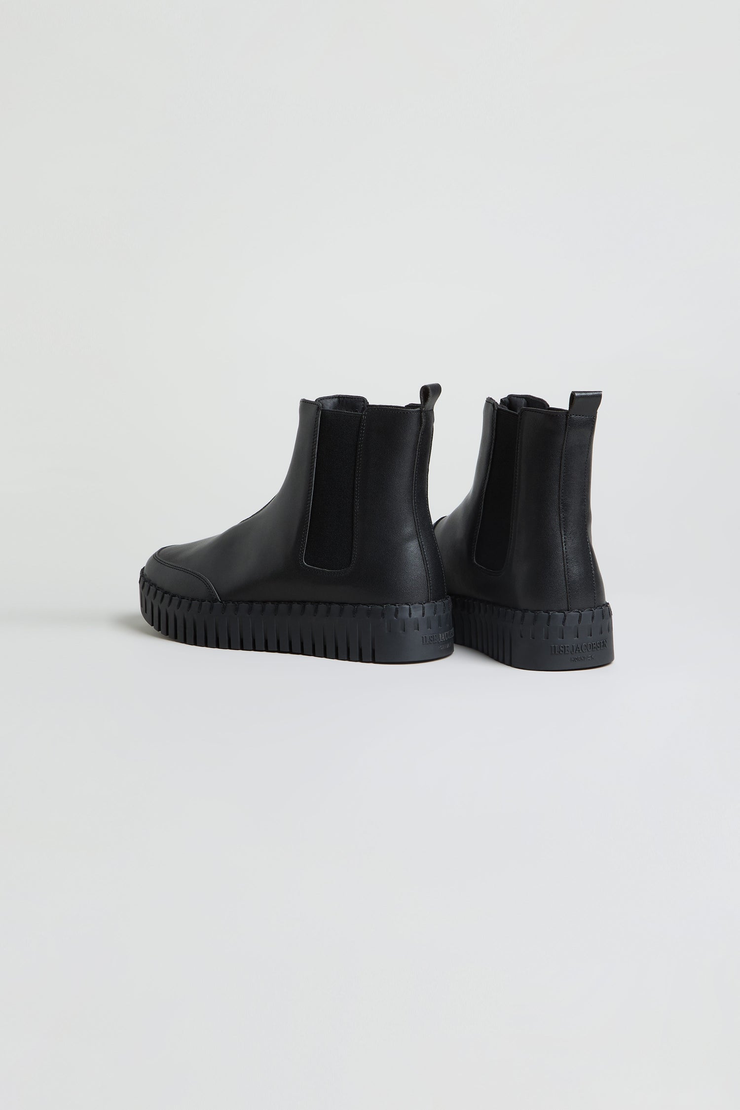 Pair of black Tulip Zip Chelsea Boots featuring elastic side panels, thick ridged soles, and a cosy faux shearling lining, positioned on a plain light background.