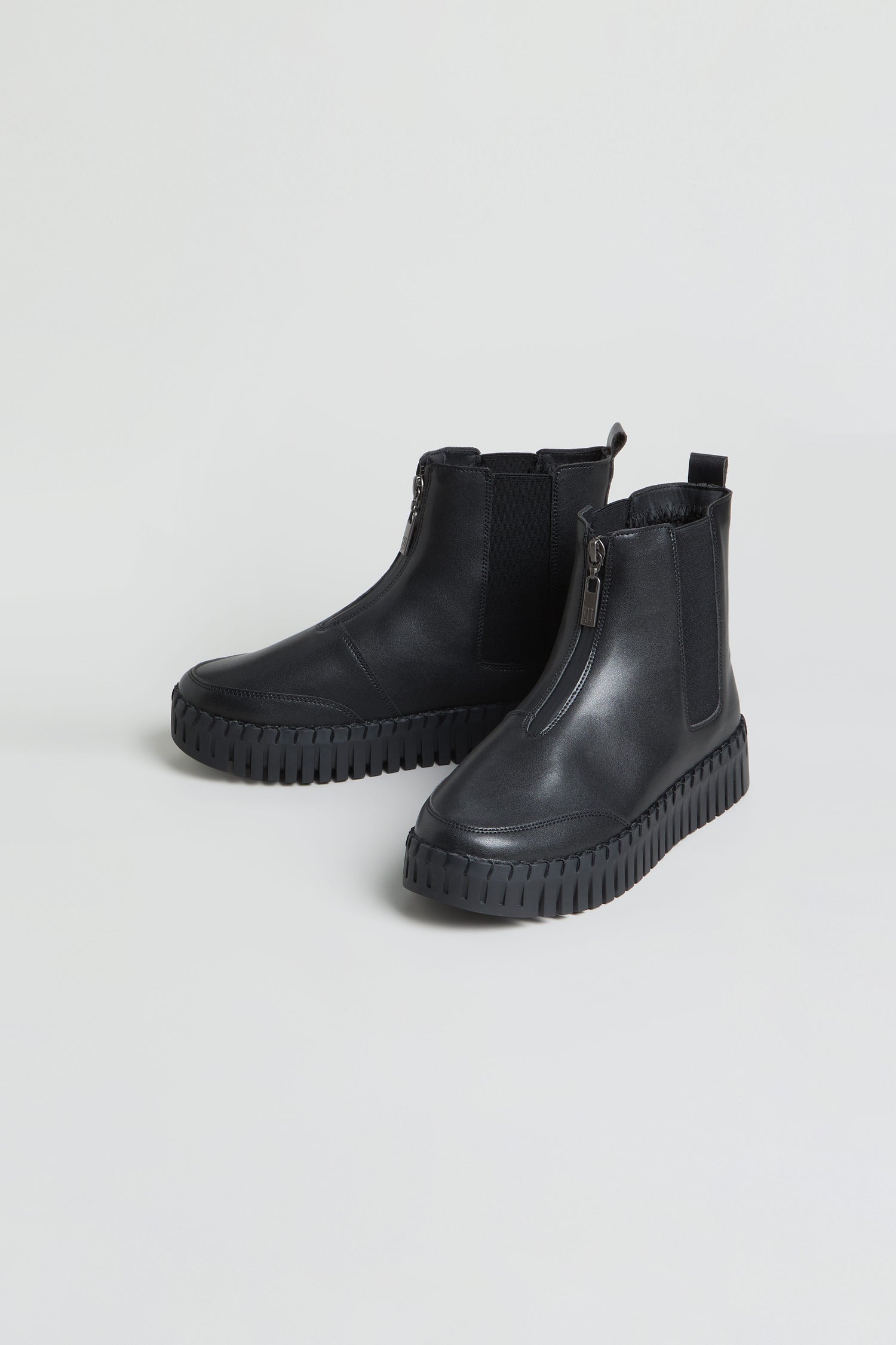 A pair of Tulip Zip Chelsea Boots in black, featuring front zippers, elastic side panels, and thick ridged soles, made from recycled microfibre and shown against a plain background.