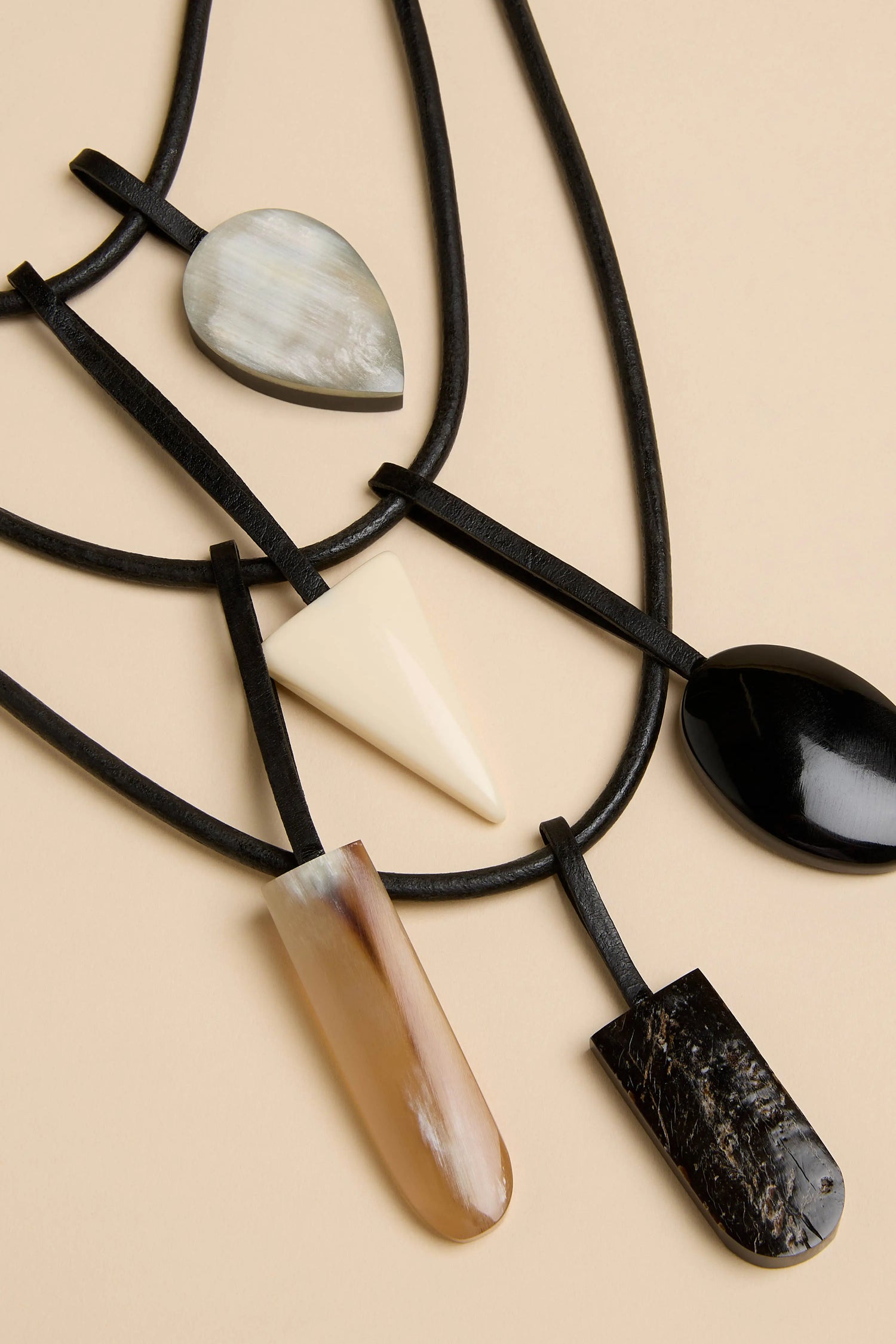 Buffalo Horn Elements Necklace featuring five multi-shaped buffalo horn pendants in shades of black, white, and tan, suspended from layered black cords.