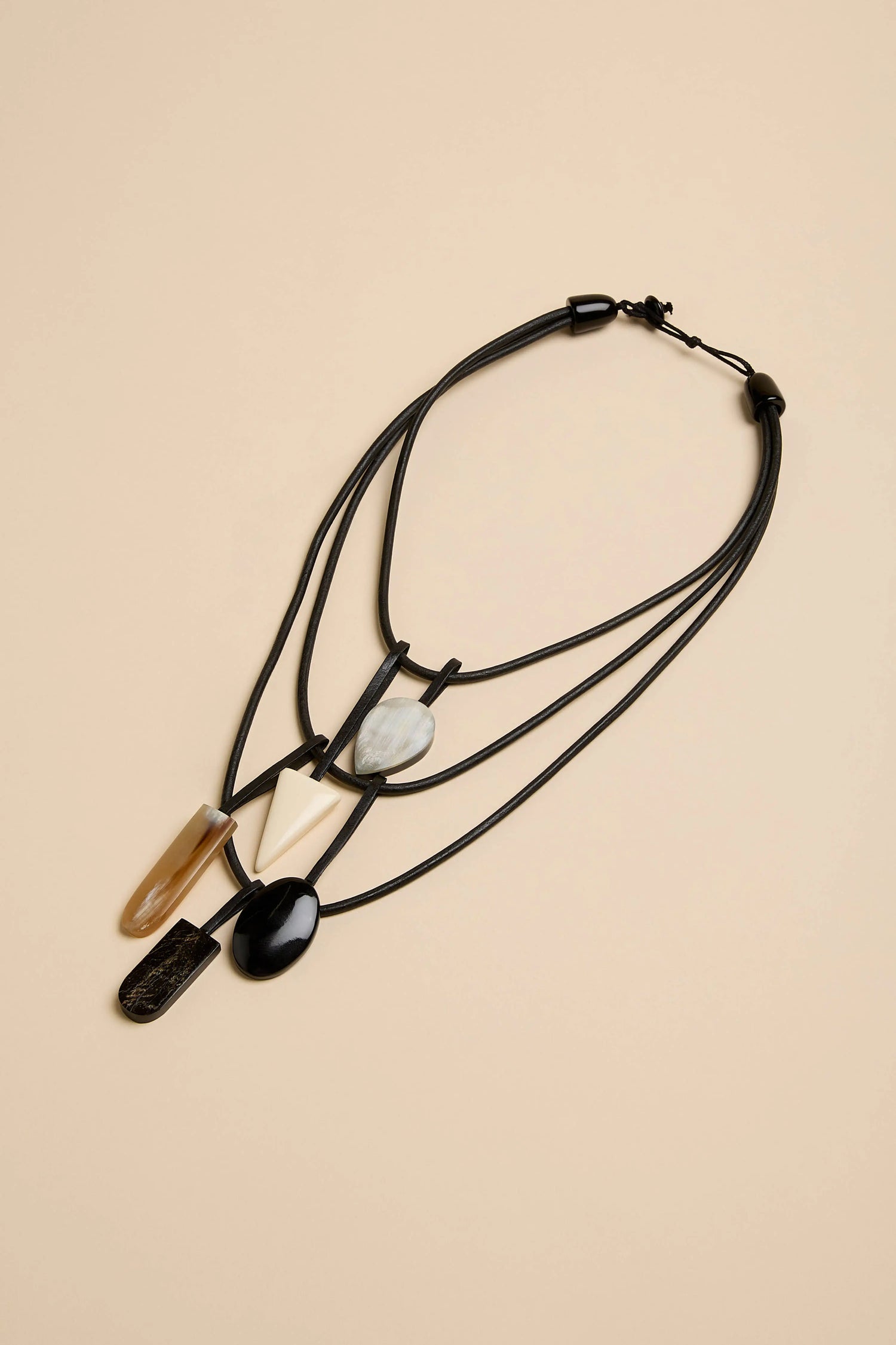 Buffalo Horn Elements Necklace featuring five assorted geometric pendants in black, white, and translucent brown on a multi-strand black cord.