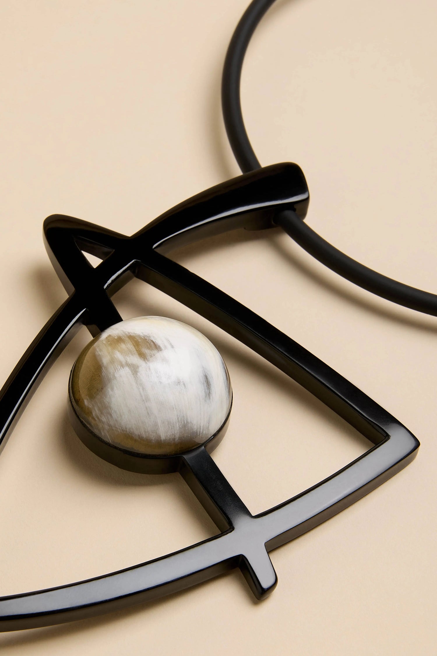 A Buffalo Horn & Resin Pendulum Necklace featuring a black buffalo horn geometric pendant with a round, marbled white and grey stone inset.