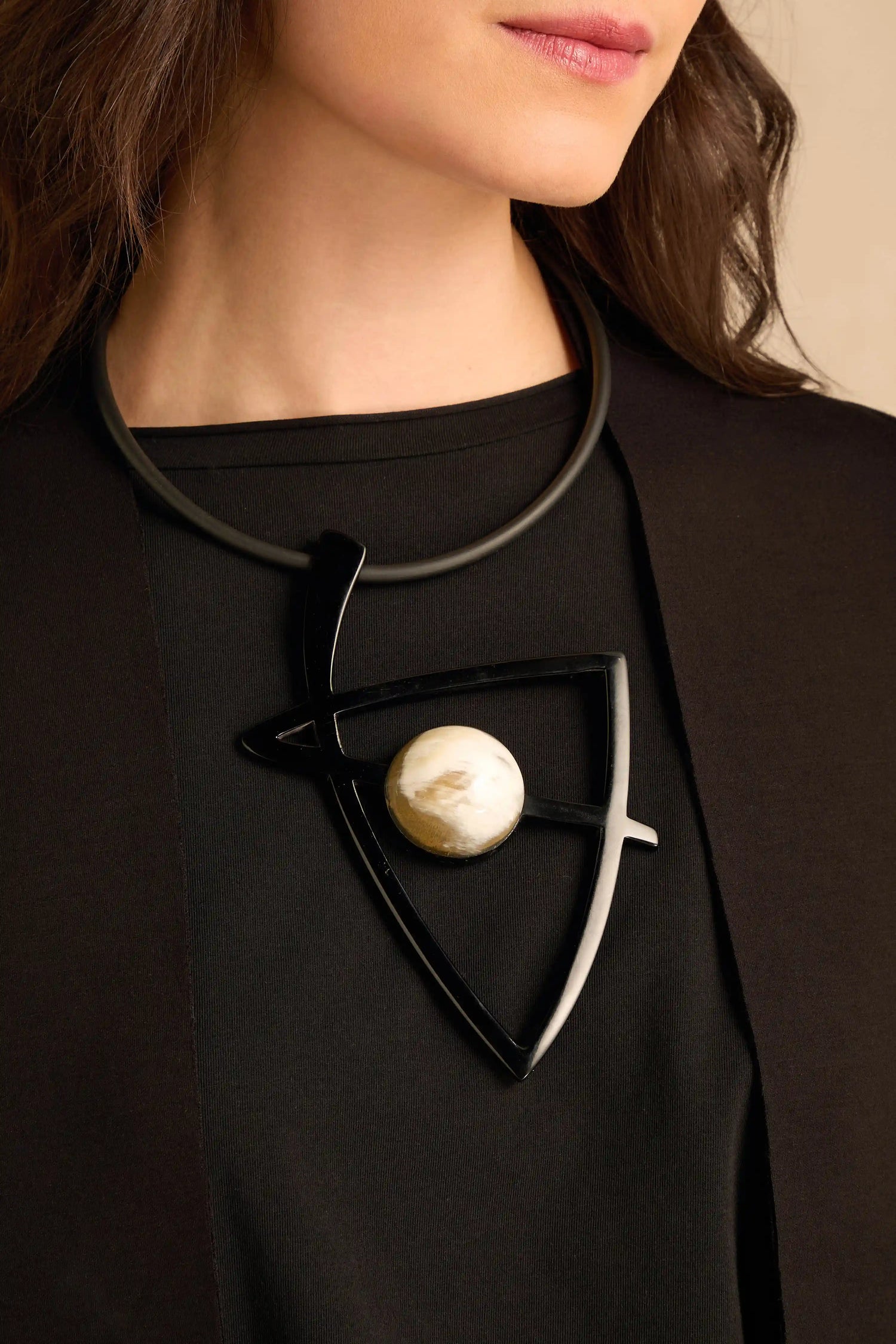A person wears a Buffalo Horn & Resin Pendulum Necklace, featuring a black geometric pendant with a circular, marbled-patterned centerpiece on a black cord.