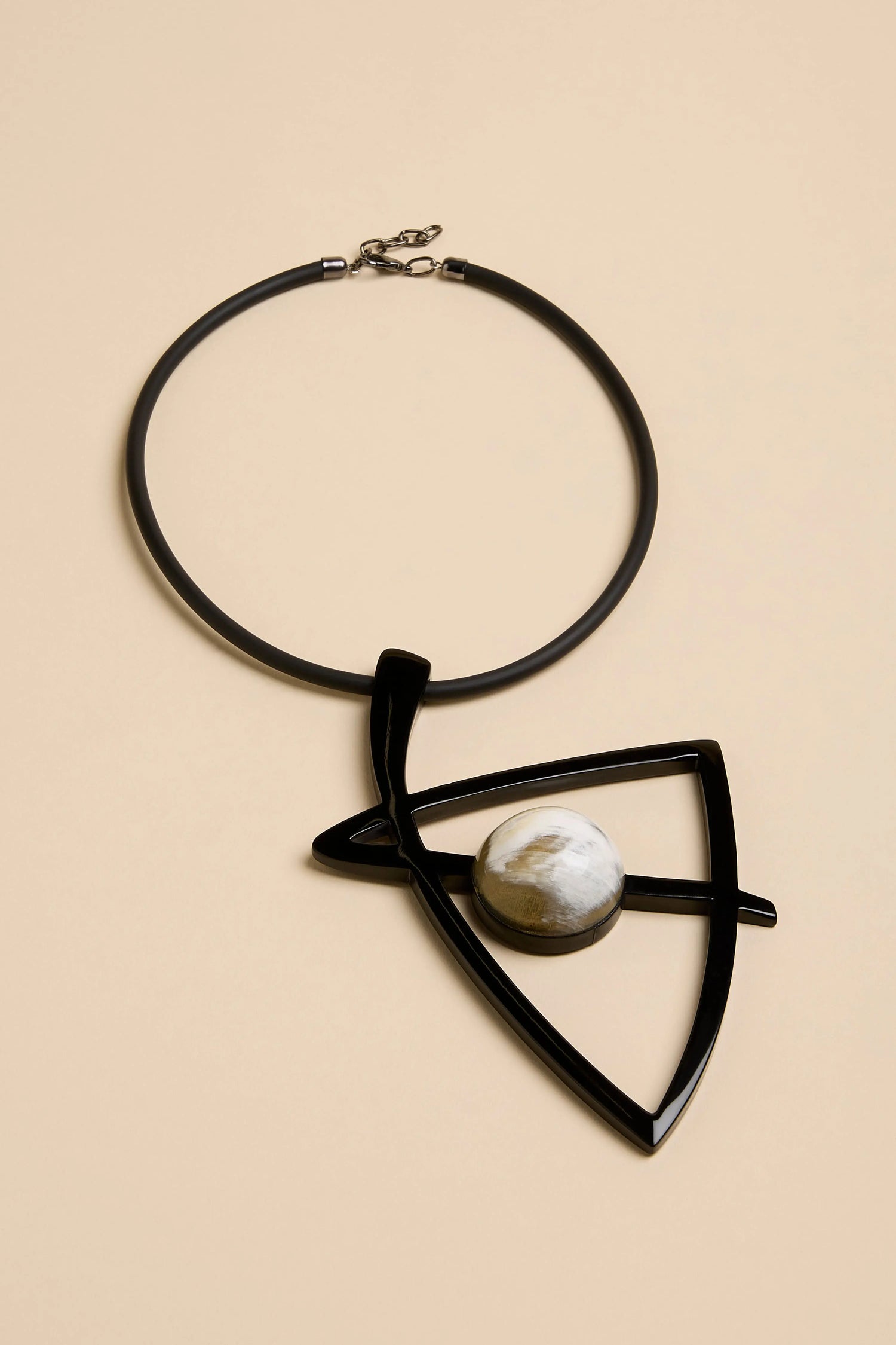 A Buffalo Horn & Resin Pendulum Necklace with a black cord and a large, black, geometric pendant featuring a spherical, marbled inlay.