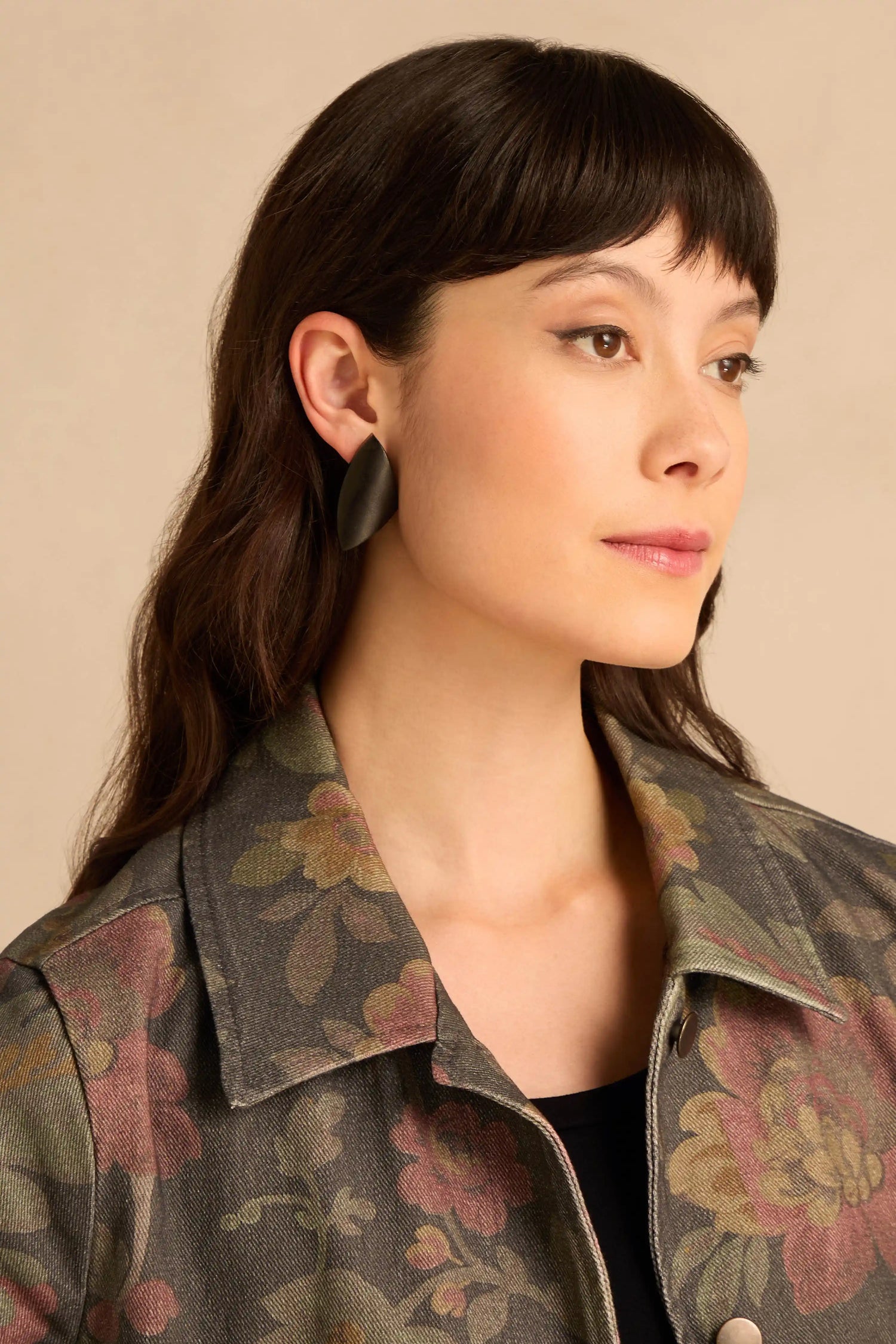 A person wearing Sculptural Mango Black Wood Earrings, featuring smooth, curved black wood.