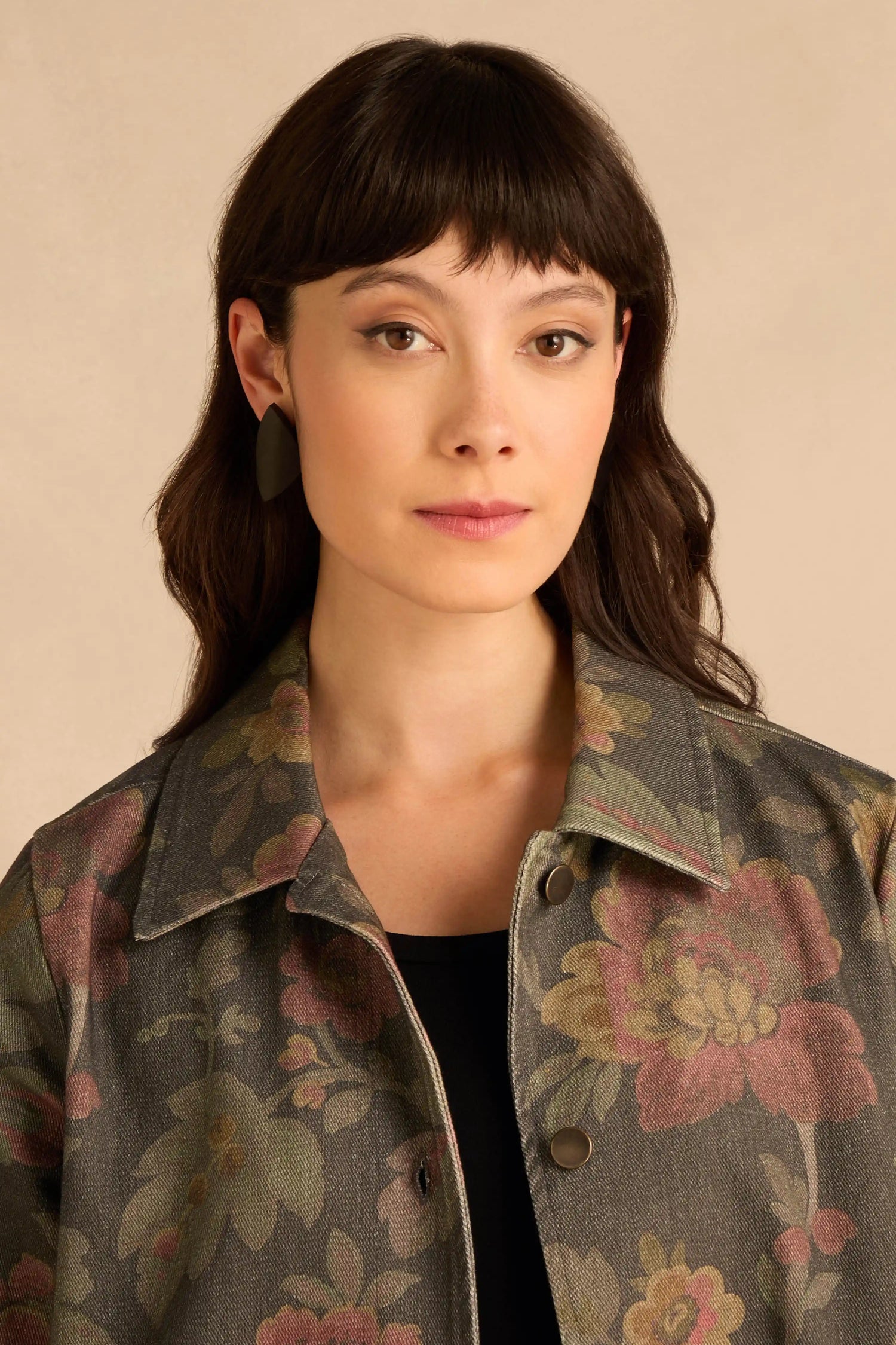 A person wearing Sculptural Mango Black Wood Earrings featuring large, matte black, petal-shaped sculptural designs.